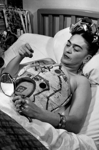 Frida in her hospital bed, drawing on her cast with the help of a mirror